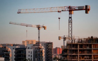 Grúas de construcción junto a edificios residenciales de obra nueva que representan la escasez de vivienda, el crecimiento urbanístico y la situación del mercado inmobiliario en España.